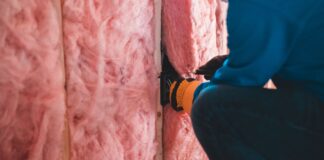Pracownik w rękawicach montuje różową wełnę mineralną w domu