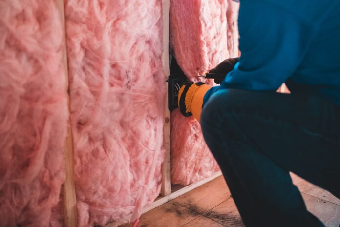 Pracownik w rękawicach montuje różową wełnę mineralną w domu