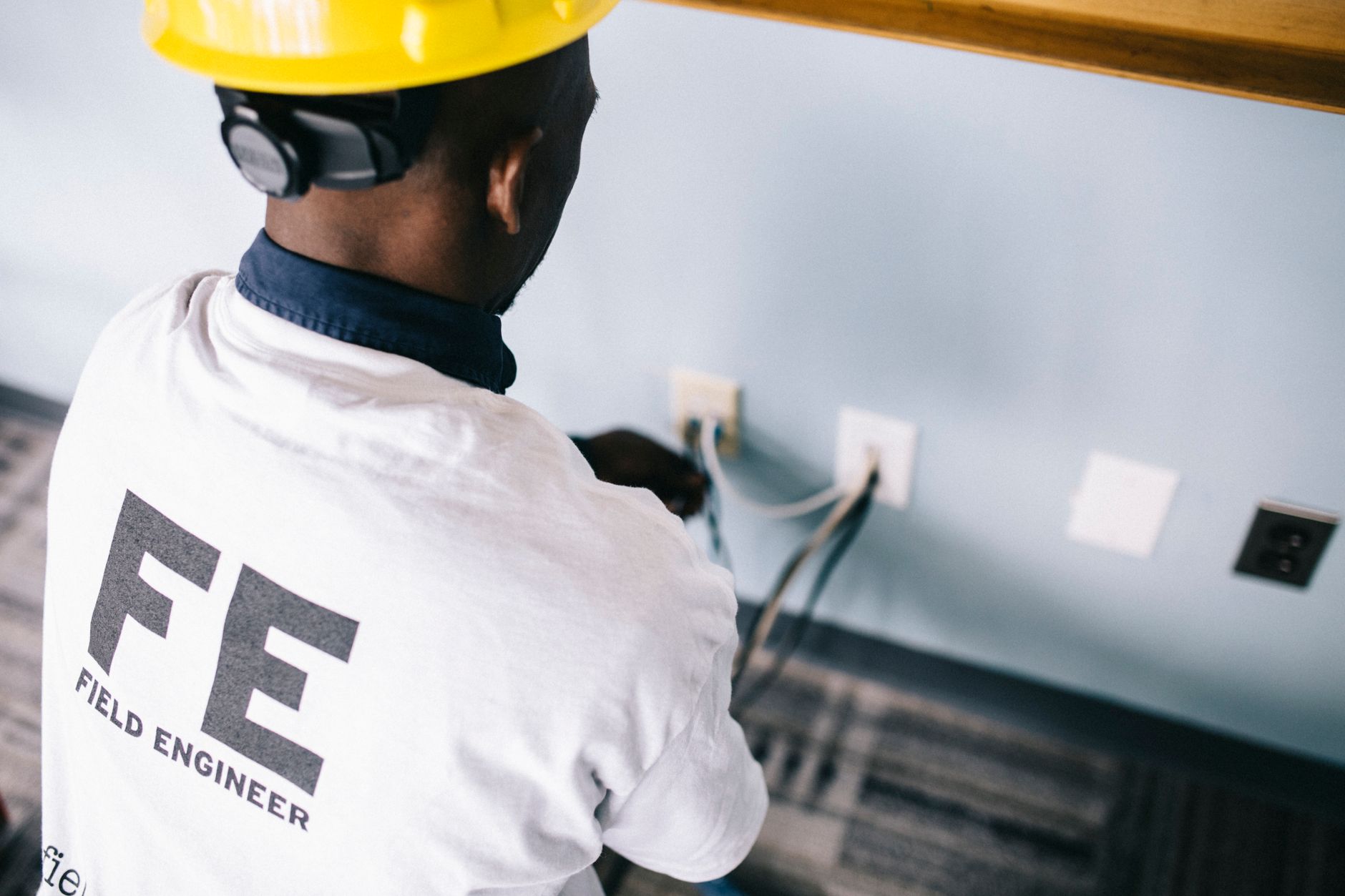 Elektryk w kasku mierzy napięcie w gniazdach ściennych testerem